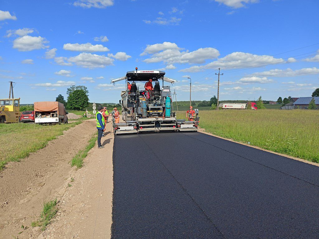 Rozściełacz układający nową warstwę asfaltu na drodze w otoczeniu pracowników budowlanych
