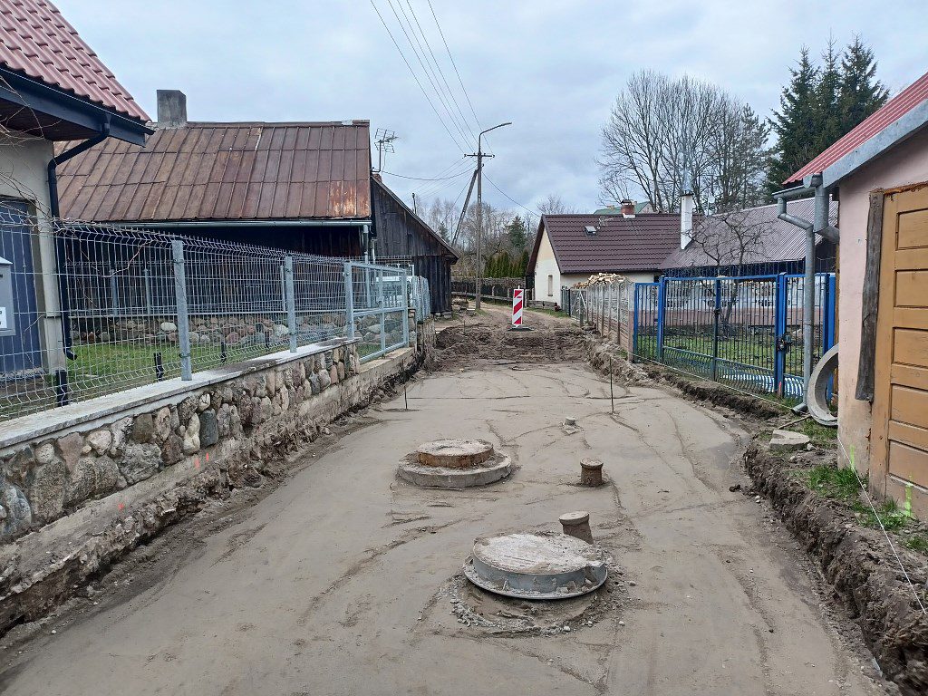 Piaszczysta droga w trakcie budowy z wystającymi włazami studzienek kanalizacyjnych