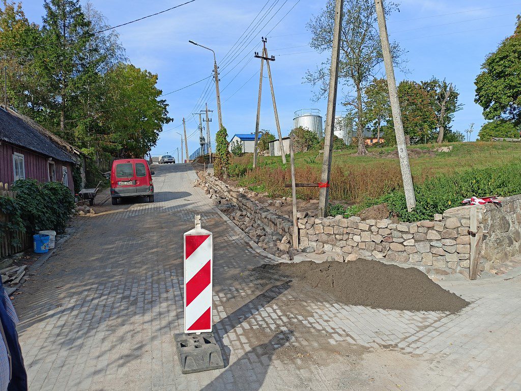 Remont wiejskiej drogi z biało-czerwonym słupkiem ostrzegawczym i budowanym kamiennym murkiem