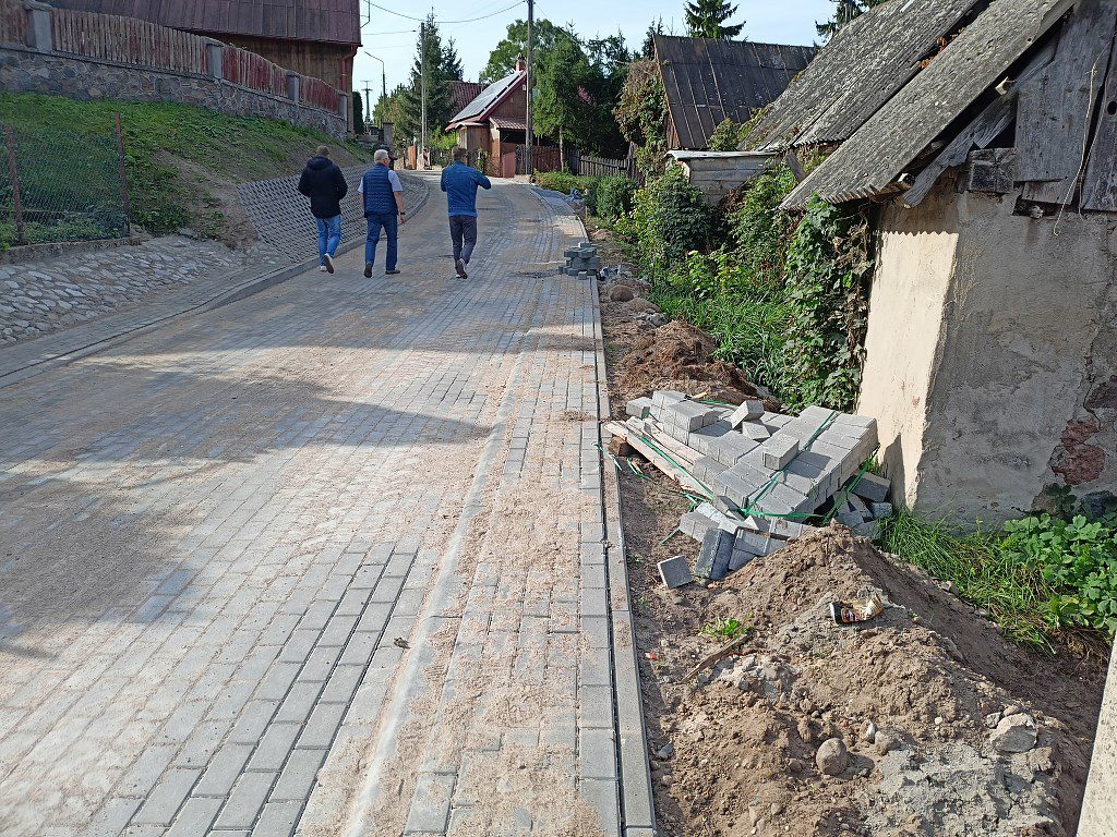 Trzej mężczyźni idą nowo wybrukowaną drogą z kostki w wiejskiej okolicy