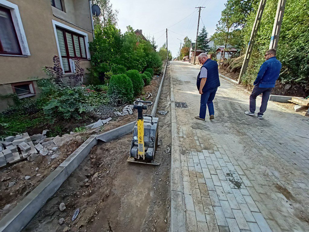 Dwaj mężczyźni wizytujący budowę drogi i chodnika z nowymi krawężnikami i zagęszczarką