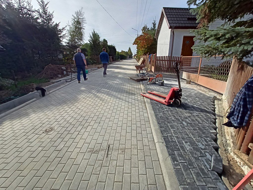 Nowo wybrukowana ulica z szarej kostki, obok narzędzia budowlane i dwaj idący mężczyźni