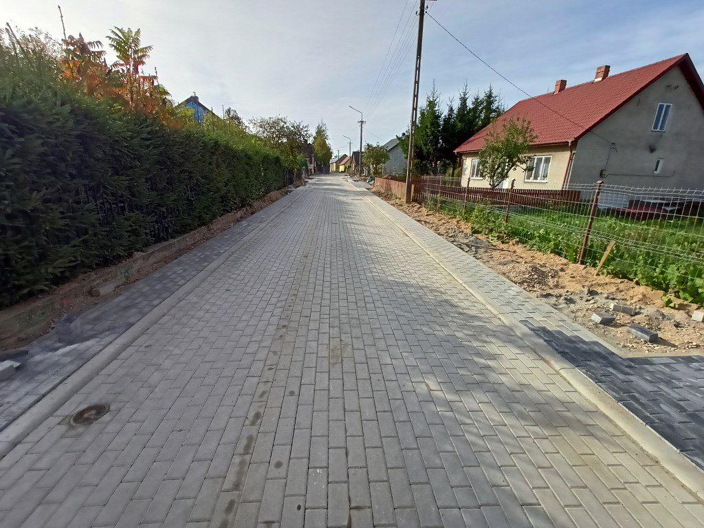 Nowa ulica wyłożona szarą kostką brukową w otoczeniu domów jednorodzinnych i zieleni