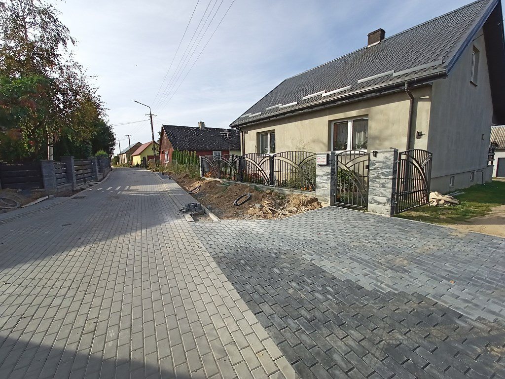 Ulica z kostki brukowej oraz dom z nowym podjazdem i ozdobnym metalowym ogrodzeniem