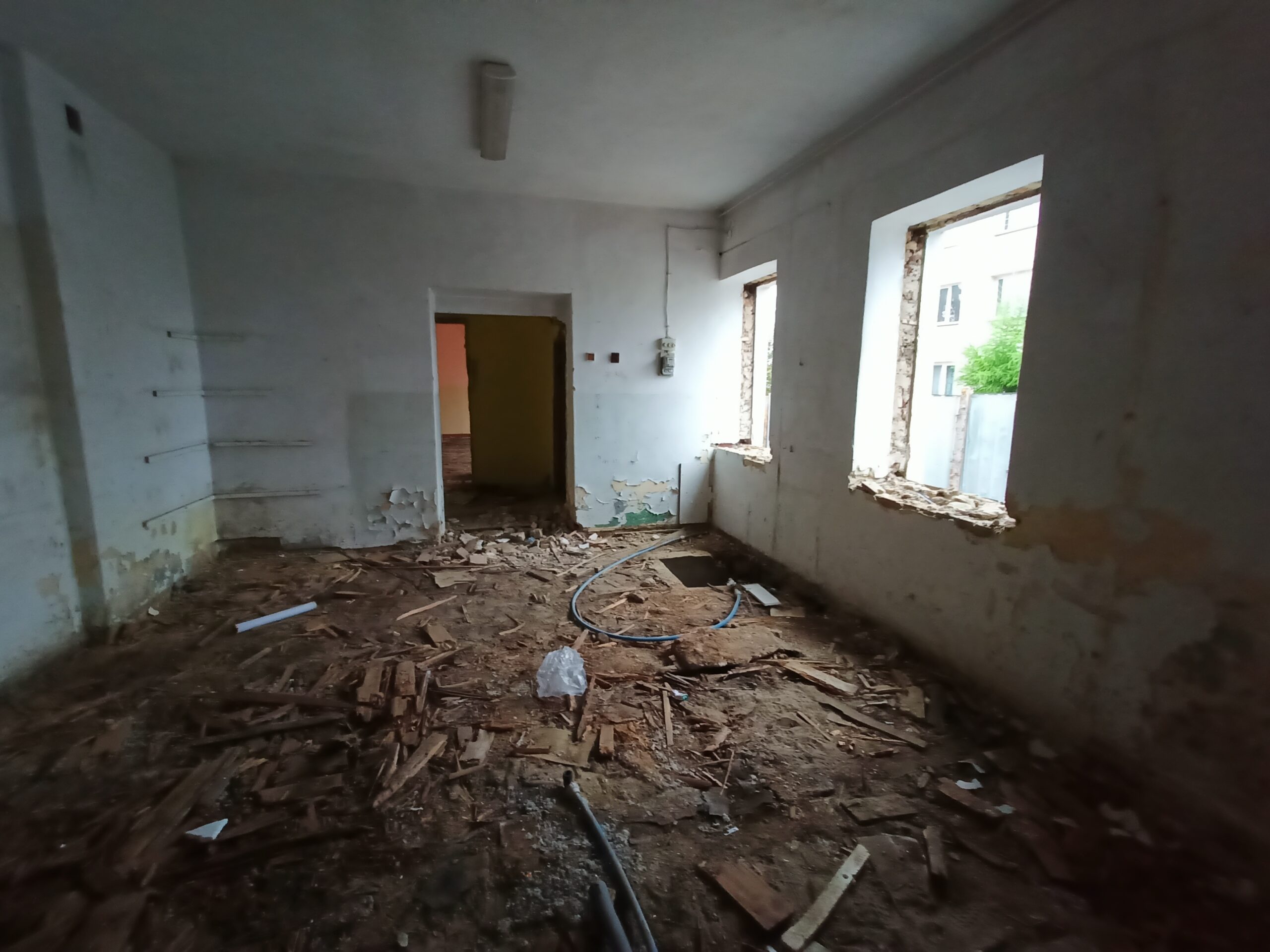 Wnętrze zniszczonego pokoju z gruzem na podłodze i oknami bez ram w trakcie remontu