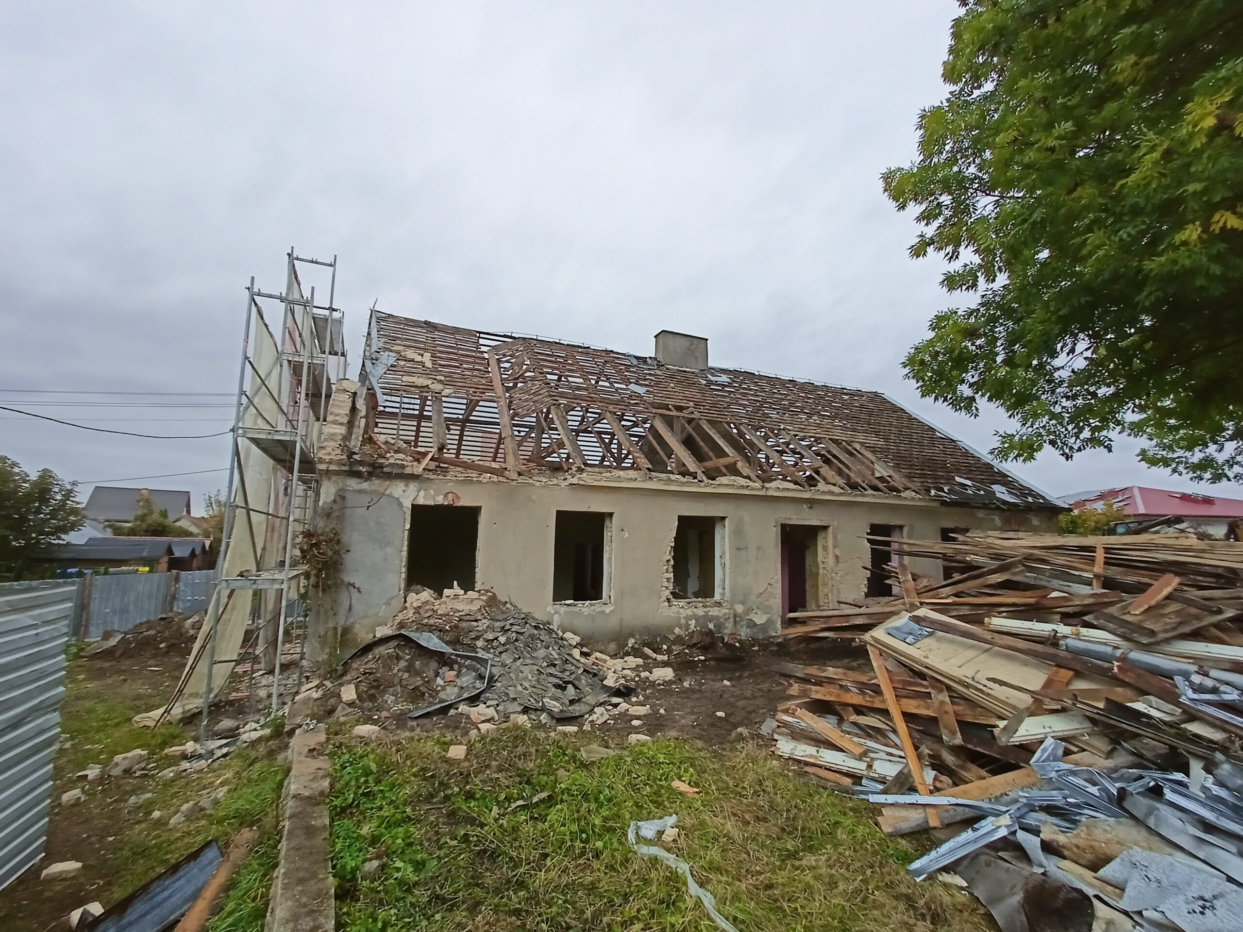 Stary dom w trakcie rozbiórki z odsłoniętą konstrukcją dachu i stertami gruzu