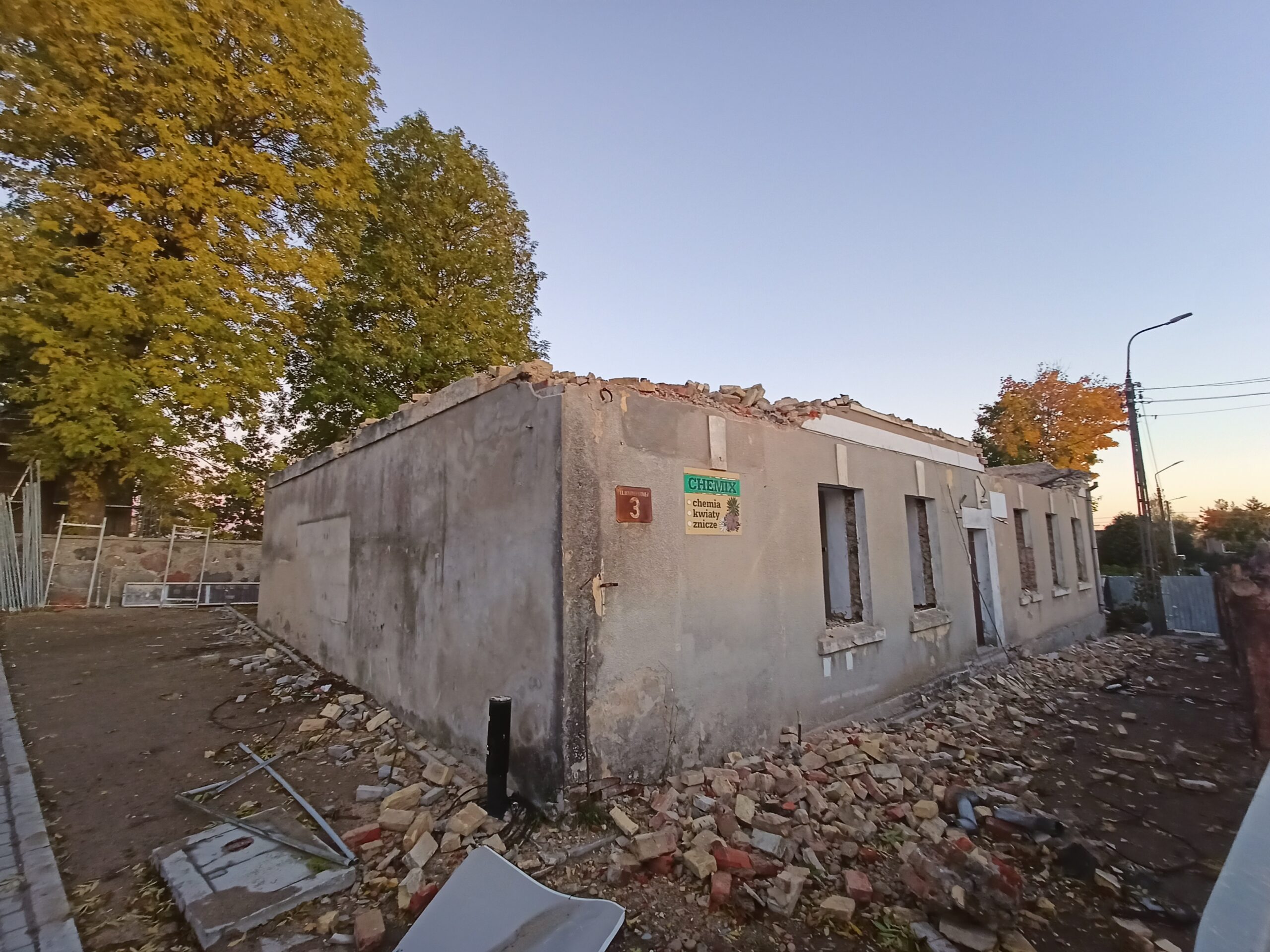 Parterowy budynek w trakcie rozbiórki, bez dachu, otoczony gruzem. Na ścianie szyld sklepu Chemix i numer 3