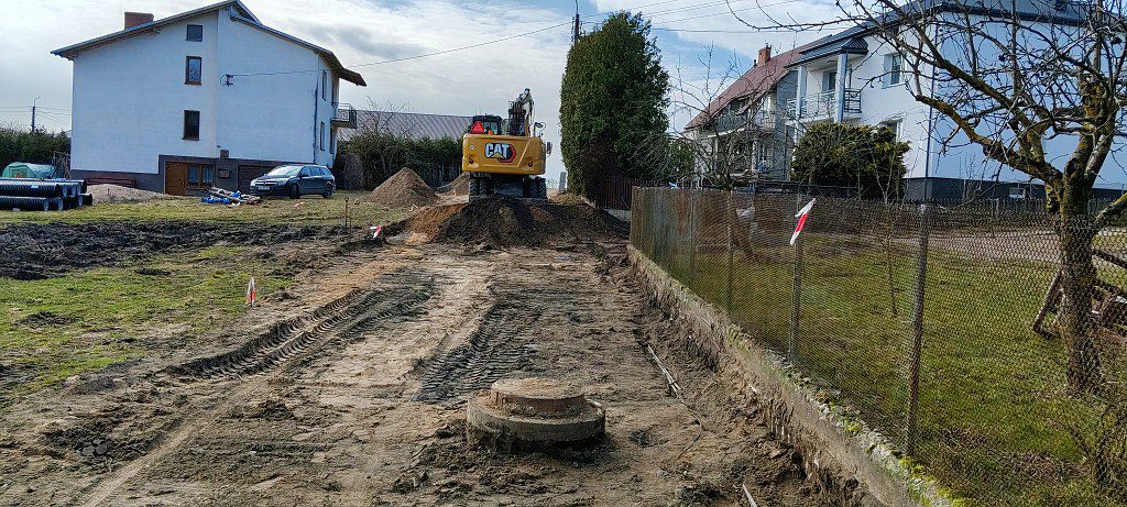 Żółta koparka CAT na placu budowy drogi między domami jednorodzinnymi