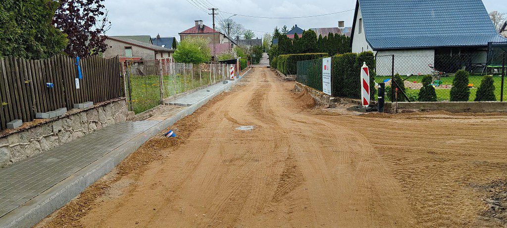 Budowa drogi i chodnika w terenie zabudowanym; piaszczysta nawierzchnia i nowo ułożona kostka brukowa