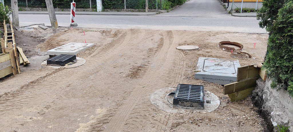 Plac budowy z nowymi włazami kanalizacyjnymi i kratkami ściekowymi na piaszczystym podjeździe