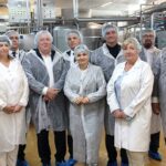 Grupa osób w odzieży ochronnej na tle maszyn w zakładzie produkcyjnym