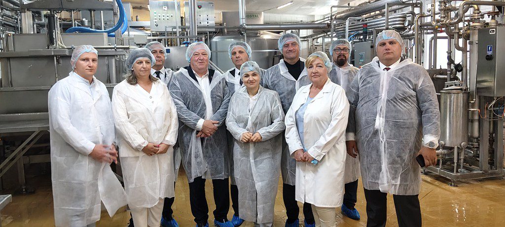 Grupa osób w odzieży ochronnej na tle maszyn w zakładzie produkcyjnym