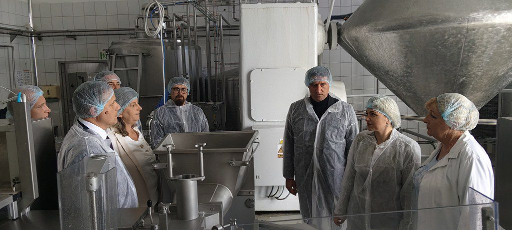 Grupa osób w odzieży ochronnej zwiedzająca halę produkcyjną z maszynami przemysłowymi