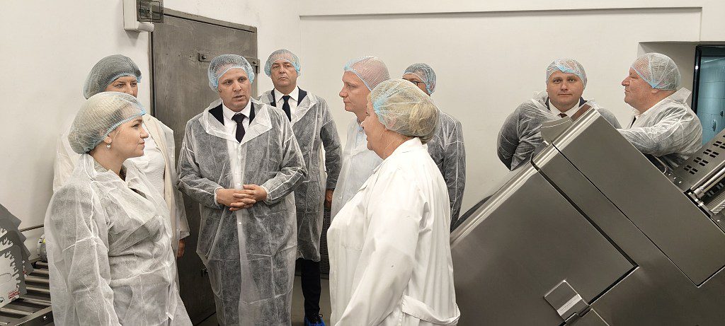Grupa osób w odzieży ochronnej i czepkach zwiedzająca zakład produkcyjny