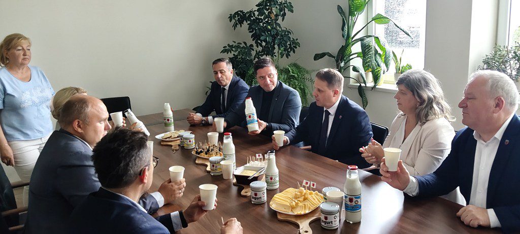 Spotkanie przy stole konferencyjnym z produktami mlecznymi; jeden z mężczyzn prezentuje butelkę