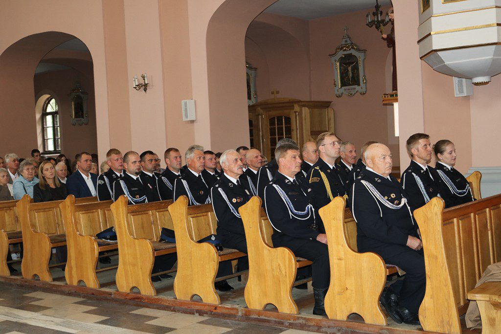 Strażacy w mundurach galowych siedzący w ławkach kościelnych podczas uroczystości