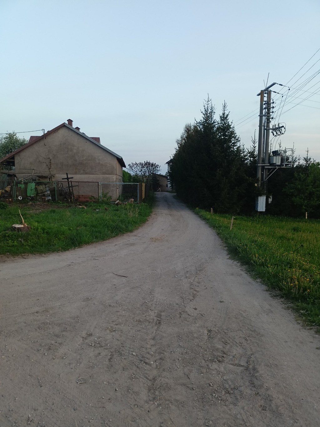 Piaszczysta wiejska droga prowadząca obok domu i słupa energetycznego z transformatorem