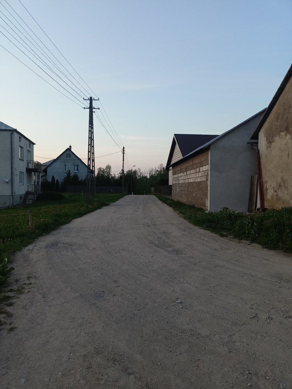 Piaszczysta droga wiejska między domami a budynkiem gospodarczym o zmierzchu