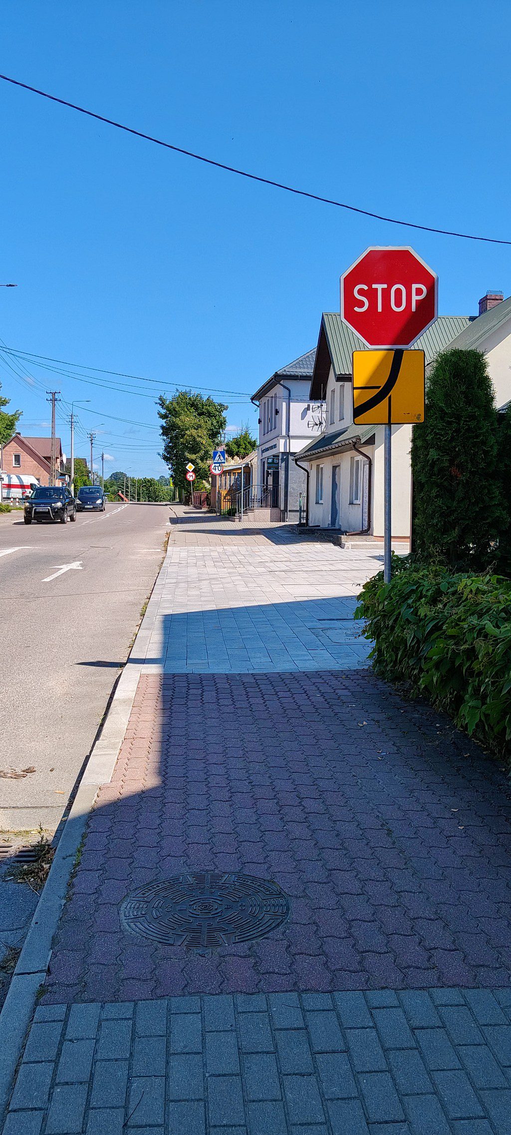 Znak STOP z tabliczką przebiegu drogi z pierwszeństwem przy chodniku wzdłuż miejskiej ulicy