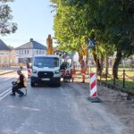 Prace drogowe w Filipowie: robotnicy i biały furgonetka na jezdni obok drogowskazów do lokalnych zabytków