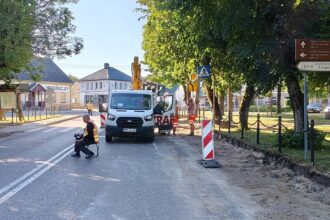 Prace drogowe w Filipowie: robotnicy i biały furgonetka na jezdni obok drogowskazów do lokalnych zabytków
