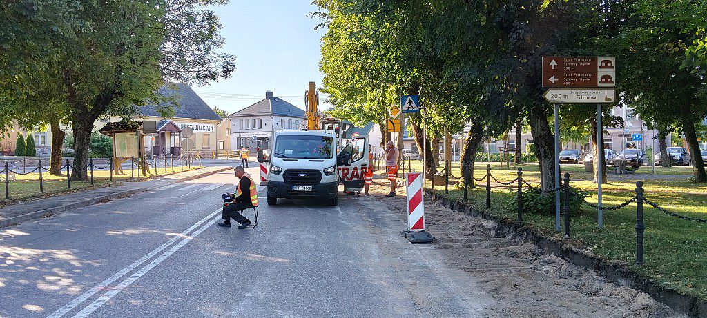 Prace drogowe w Filipowie: robotnicy i biały furgonetka na jezdni obok drogowskazów do lokalnych zabytków