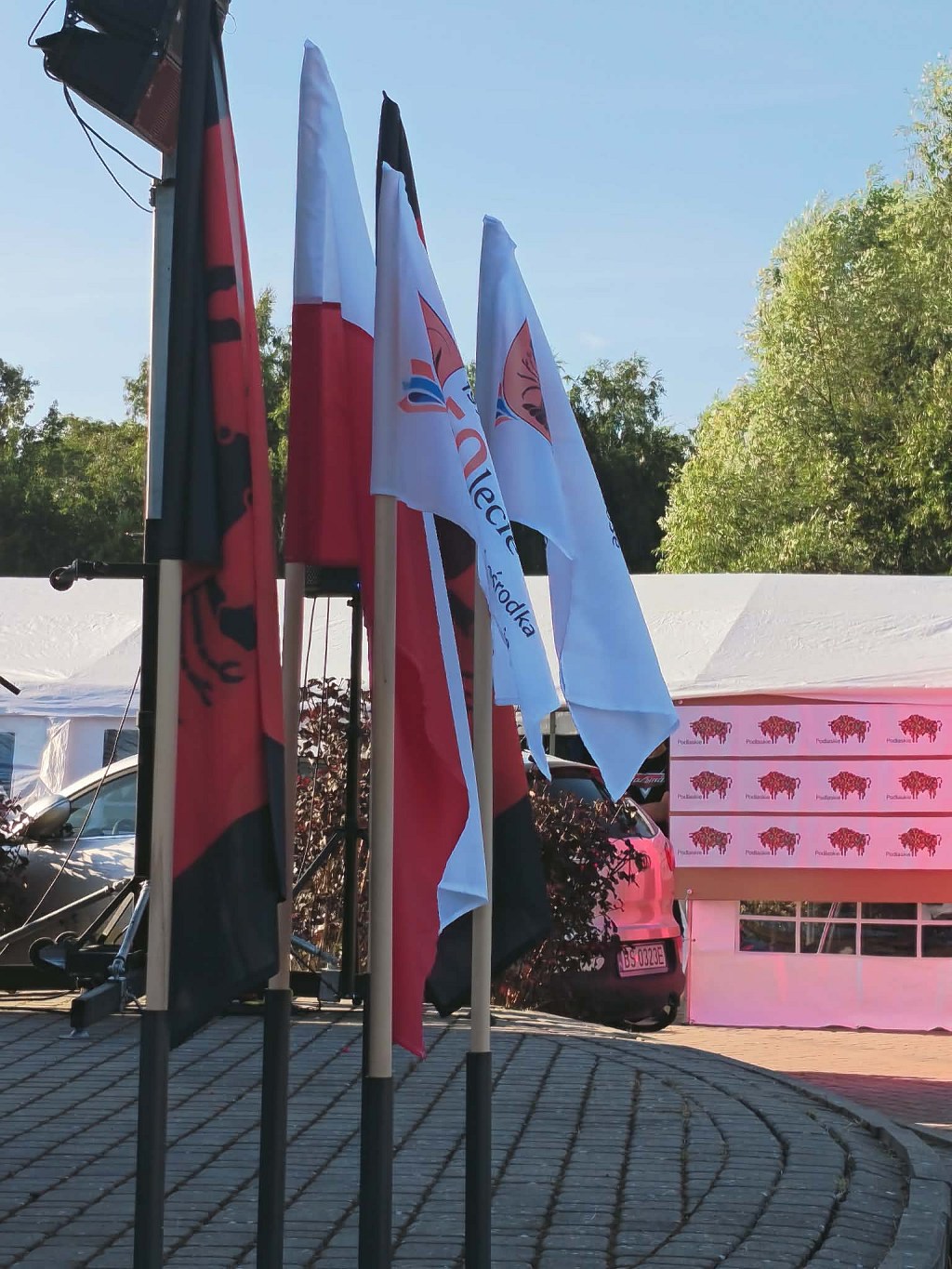 Flagi Polski oraz okolicznościowe z okazji 70-lecia Ośrodka na tle namiotu z logo województwa podlaskiego