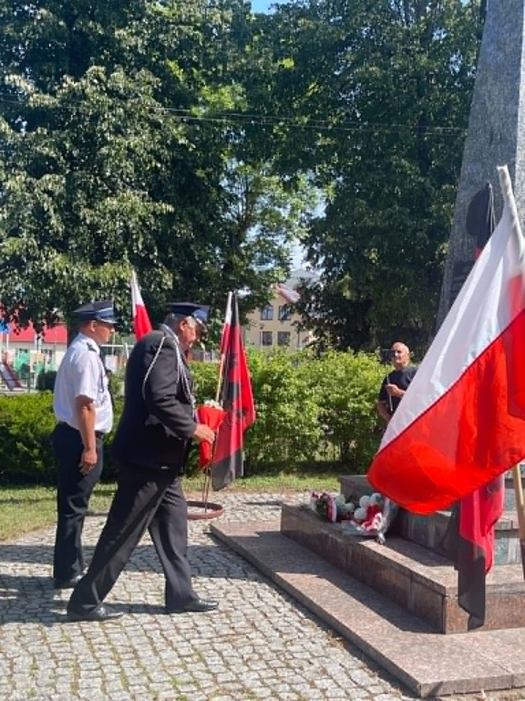 Mężczyzna w mundurze składa kwiaty pod pomnikiem w otoczeniu polskich flag