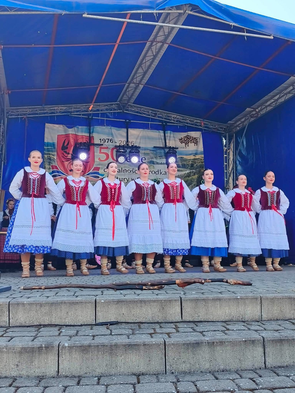 Osiem kobiet w podlaskich strojach ludowych stoi na scenie podczas jubileuszu 50-lecia ośrodka kultury