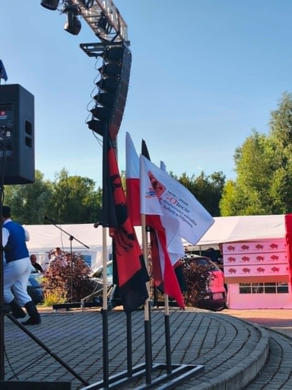 Flagi Polski, Albanii i jubileuszowa flaga 50-lecia na tle sceny podczas wydarzenia plenerowego