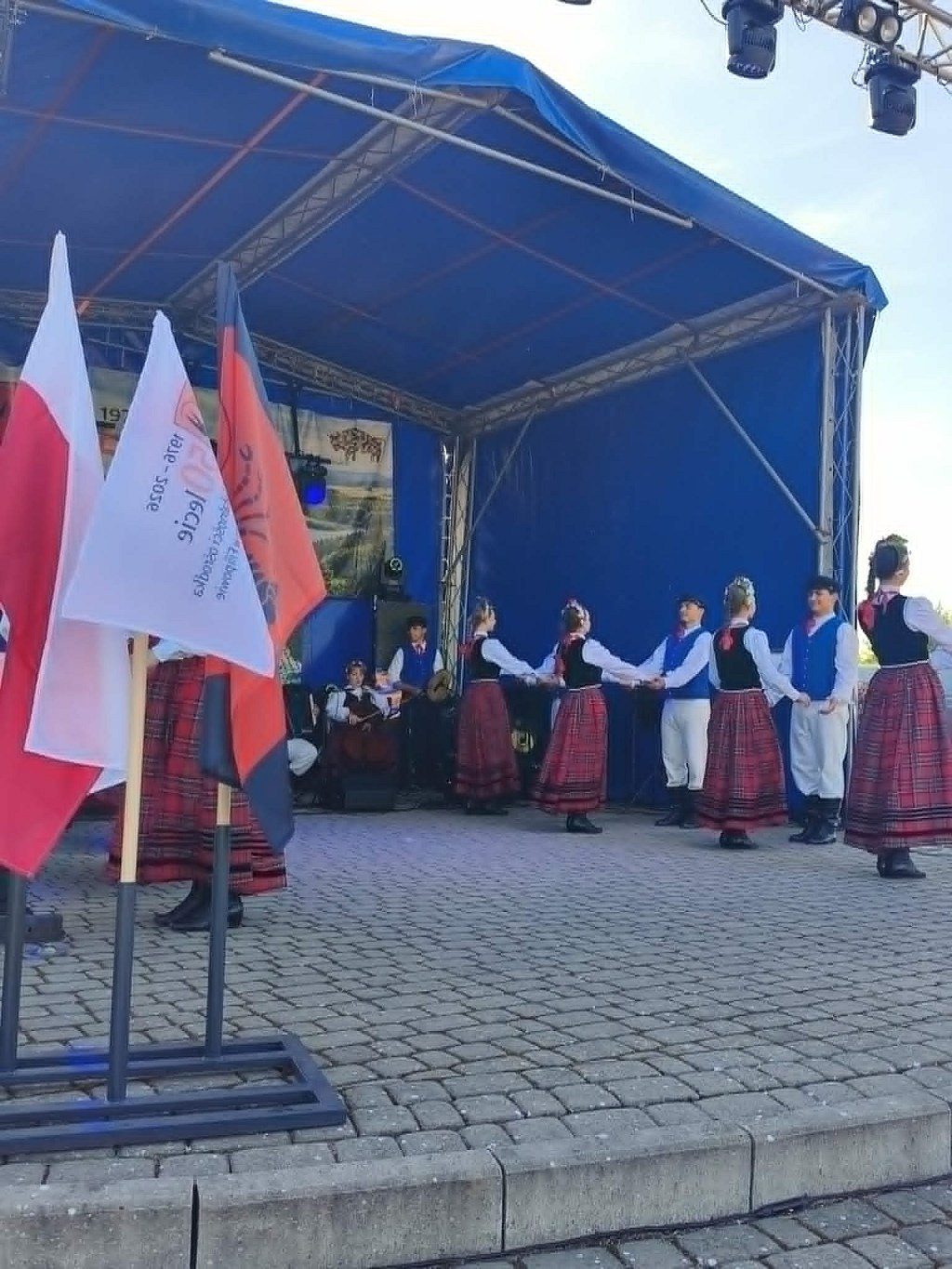 Zespół ludowy w tradycyjnych strojach tańczący na plenerowej scenie podczas lokalnego wydarzenia
