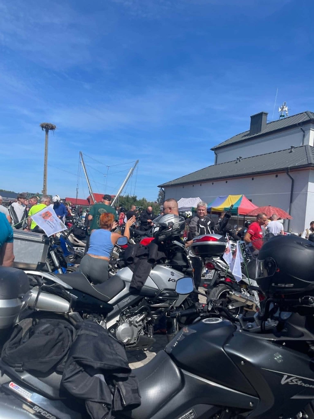 Zlot motocyklowy na placu w słoneczny dzień; liczne zaparkowane motocykle i zgromadzeni ludzie