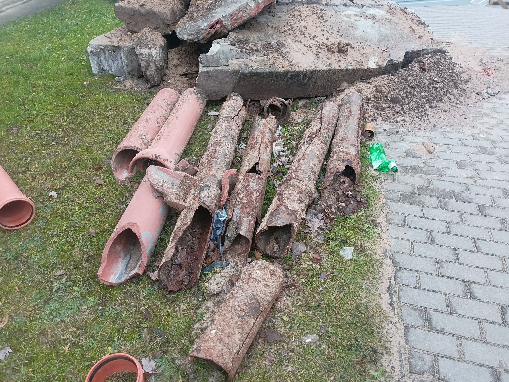 Stare, zardzewiałe i popękane rury leżące na ziemi obok gruzu i chodnika