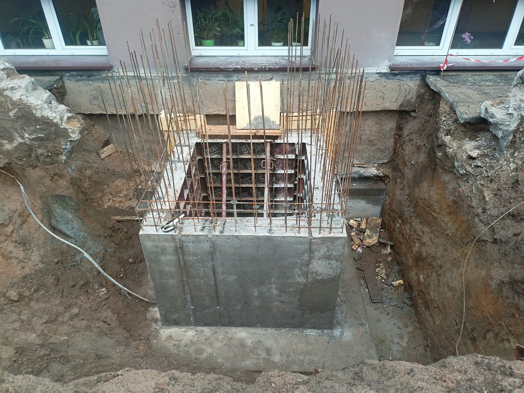 Betonowy fundament z wystającymi prętami zbrojeniowymi w wykopie przy budynku