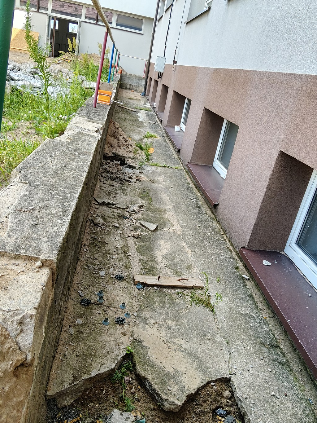 Zniszczony, popękany betonowy chodnik z ubytkami i gruzem przy ścianie budynku