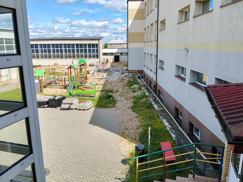 Plac zabaw przy budynku szkoły w trakcie prac remontowych, widoczne hałdy piasku i materiały budowlane