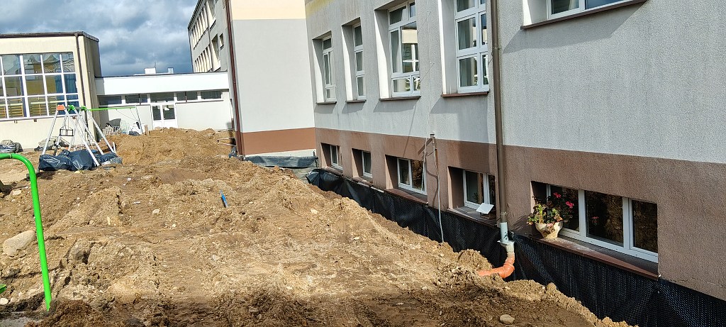 Prace przy izolacji fundamentów budynku: odkopana ziemia i czarna folia kubełkowa na ścianach