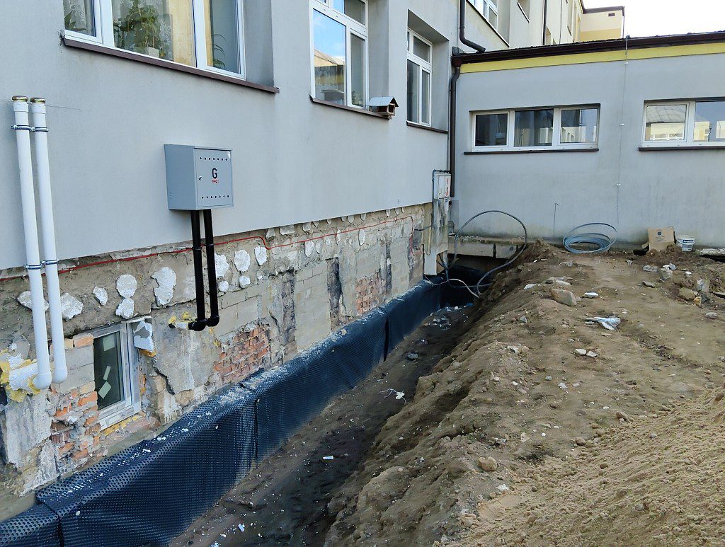 Odkryte fundamenty budynku z nałożoną czarną folią kubełkową wzdłuż wykopu