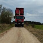 Czerwona ciężarówka MAN z podniesioną wywrotką na wiejskiej drodze gruntowej