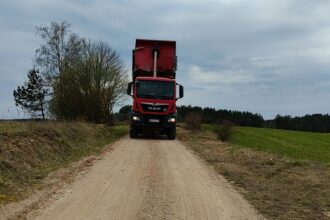 Czerwona ciężarówka MAN z podniesioną wywrotką na wiejskiej drodze gruntowej