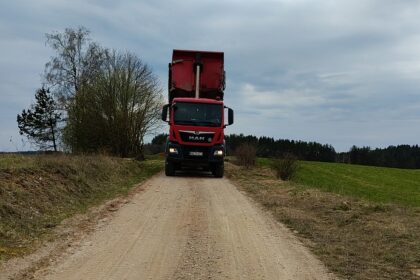 Czerwona ciężarówka MAN z podniesioną wywrotką na wiejskiej drodze gruntowej