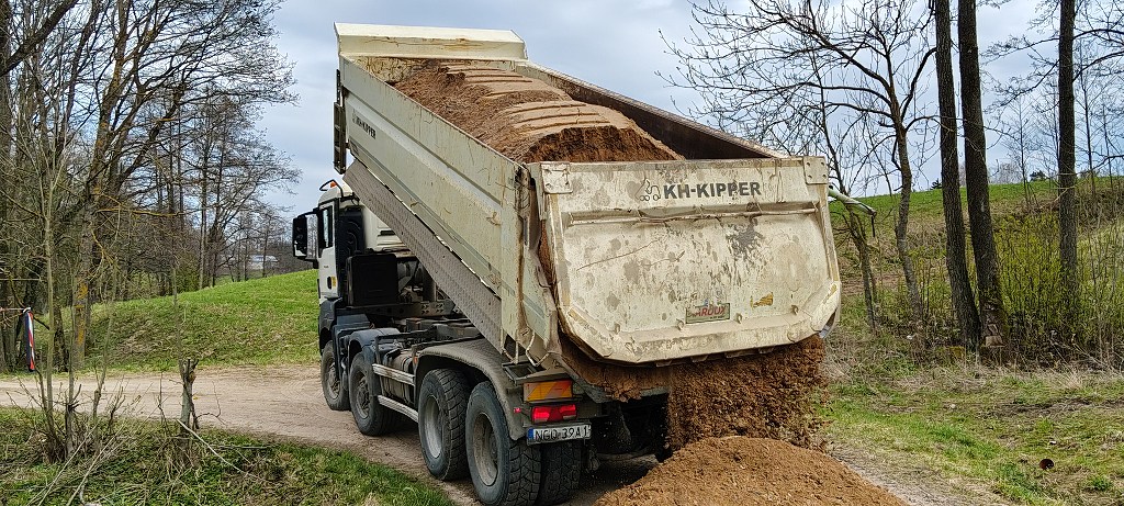 Biała ciężarówka wywrotka wysypuje ziemię na gruntową drogę