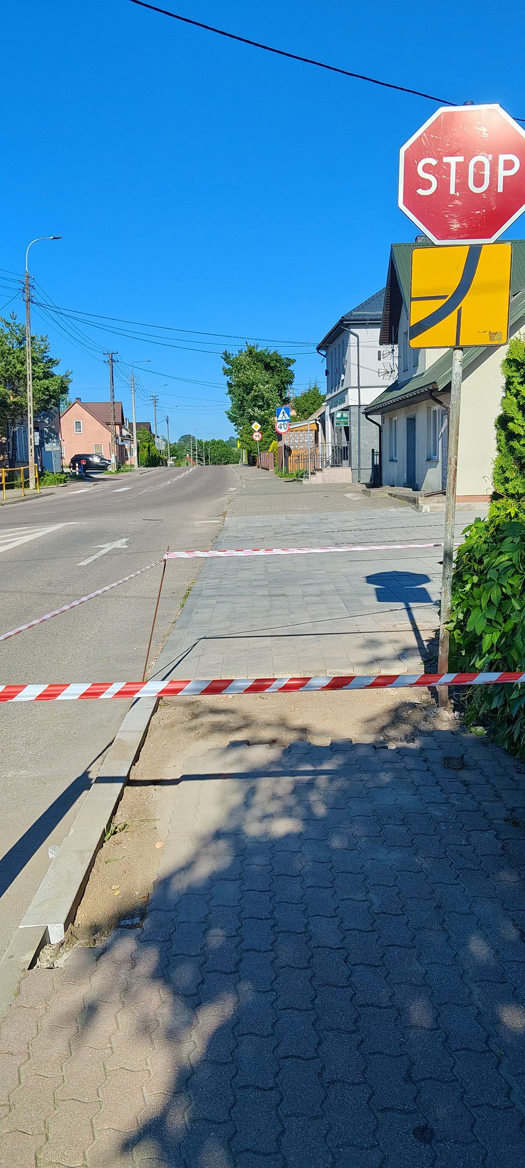 Chodnik zagrodzony biało-czerwoną taśmą ostrzegawczą przy skrzyżowaniu ze znakiem STOP
