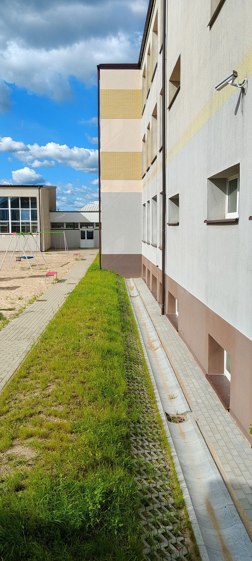 Elewacja budynku z betonowym kanałem odpływowym, pasem trawy i placem zabaw w tle