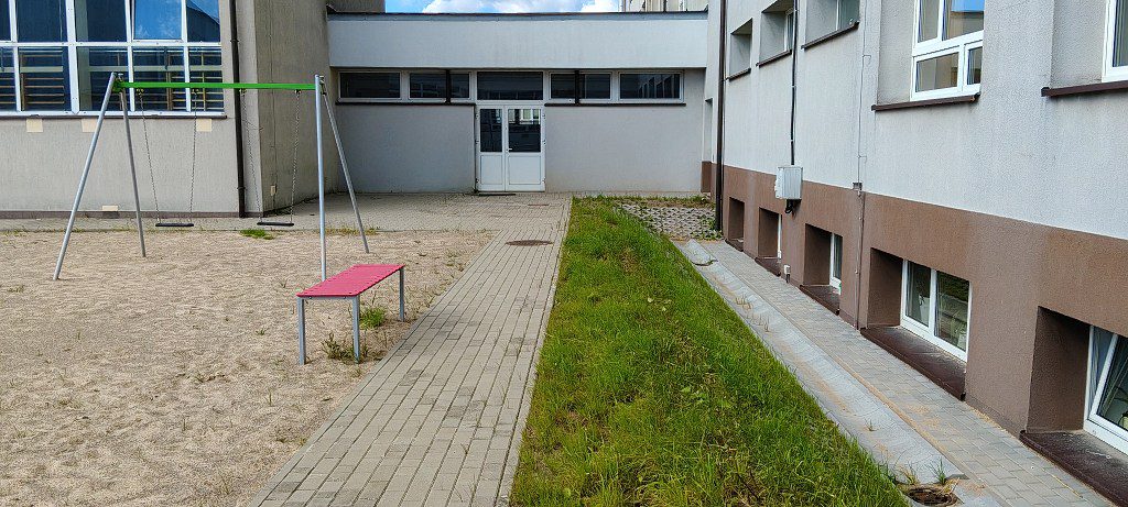 Plac zabaw z huśtawką i czerwoną ławką przy budynku