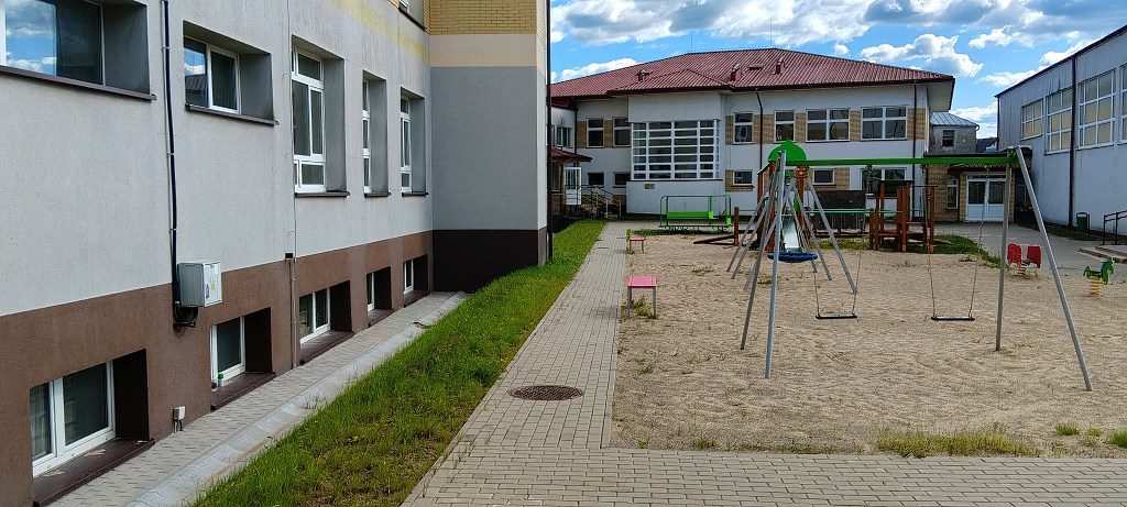 Budynek szkoły z placem zabaw wyposażonym w huśtawki i zjeżdżalnię