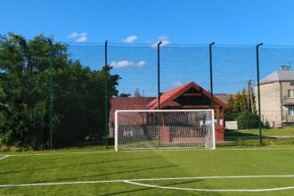 Puste boisko piłkarskie ze sztuczną nawierzchnią, bramką i wysokim ogrodzeniem w słoneczny dzień