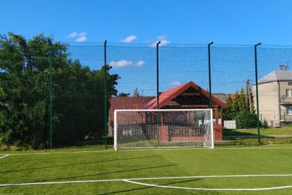 Puste boisko piłkarskie ze sztuczną nawierzchnią, bramką i wysokim ogrodzeniem w słoneczny dzień