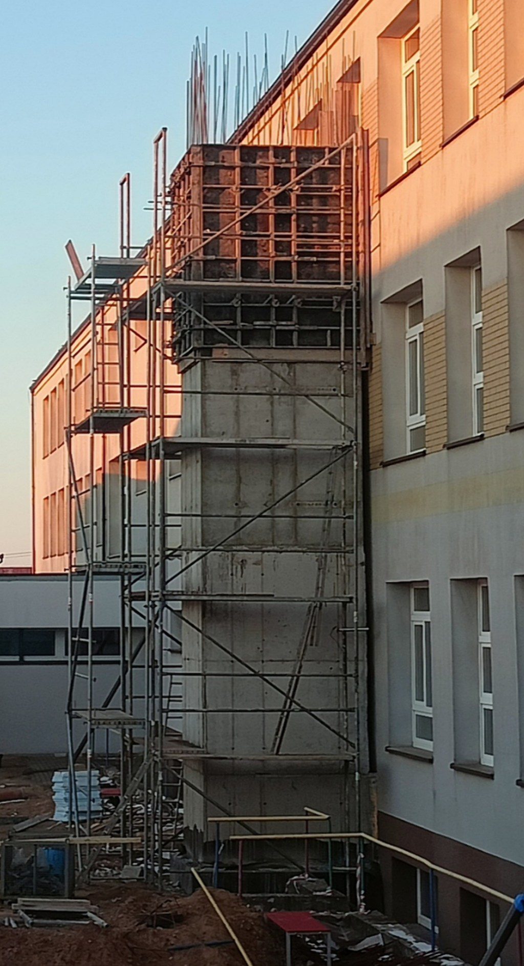 Betonowy szyb w budowie przy ścianie budynku, otoczony rusztowaniami i szalunkami