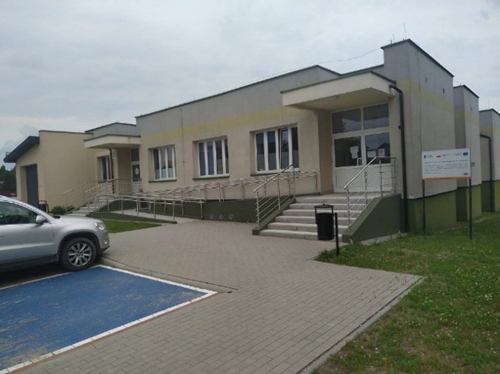 Parterowy budynek z podjazdem dla niepełnosprawnych, schodami i niebieskim miejscem parkingowym